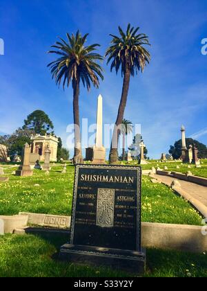 Weißer Obelisk-Grabmarker zwischen zwei Palmen. Kopfstein mit Namen Shishmanian, Kevork, Astghig. Gruft, Gräber, Gräber. Mountain View Cemetery, Oakland, Kalifornien. Stockfoto