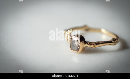 Goldener Verlobungsring mit einem Diamanten auf einem Marmortisch Stockfoto