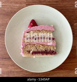 Scheibe Erdbeerkuchen, mit rosafarbenem Erdbeerfrost, SchichtenErdbeermarmeladenfüllung und Vanilleschwamm, auf weißem Teller Stockfoto