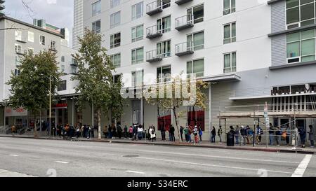 LOS ANGELES, CA, MAR 16, 2010: Menschen, die sich unter dem nahe gelegenen Gerüst aufstellen, um Lebensmittel zu bekommen, außerhalb des Ralphs Supermarktes in der Innenstadt zu Beginn der Covid-19-Pandemie in den USA. Seitenansicht. Stockfoto
