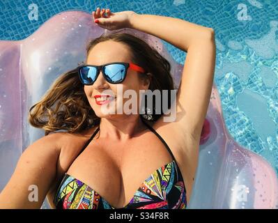 Frau, die Sonnenbrille auf einer aufblasbaren Poolmatratze trägt Stockfoto