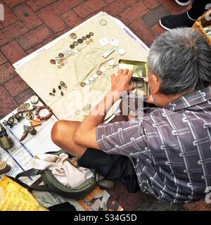 Ein Händler verkauft Metallantiqueten, Kurios und alte Münzen auf der Straße, Sham Shui Po, Kowloon, Hongkong Stockfoto