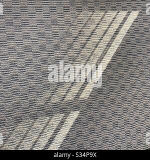 Abstrakter Hintergrund, der von der Sonne erzeugt wird, die durch Jalousien glänzt, Schatten wirft und Licht auf einen gemusterten Teppich wirft Stockfoto