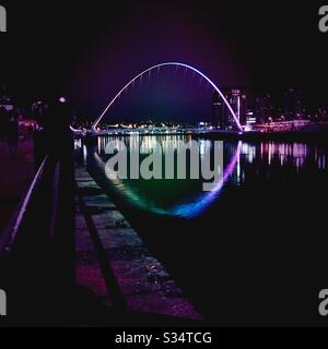 Die Architektur von Newcastle Quayside leuchtet nachts auf. Newcastle upon Tyne, North East England. Die Millennium Bridge spiegelt sich im Fluss Tyne wider Stockfoto