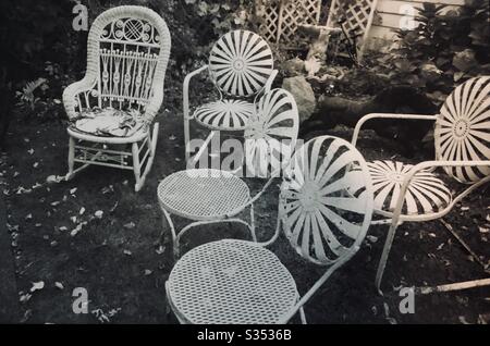 Frühlings-Garten mit Metallstühlen und Korbschaukelstuhl auf Rasen ohne Menschen auf einem Schwarz-Weiß-Foto Stockfoto