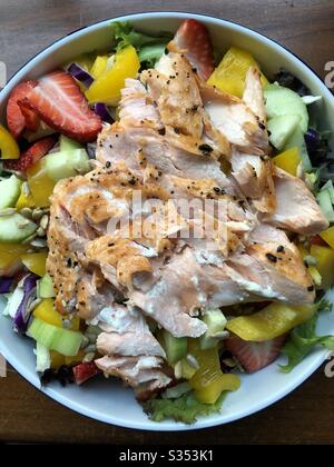 Eine Schüssel mit Salat mit gelbem Paprika, Gurke und Erdbeeren, mit gegrilltem Lachs. Stockfoto