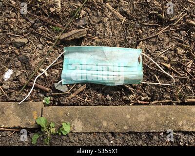 Weggeworfene chirurgische Einwegmaske, die neben einem öffentlichen Fußweg liegt. Eine neue Umweltverschmutzung. Stockfoto