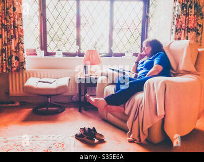 Eine Dame sitzt in einem bequemen Sessel im Wohnzimmer. Stockfoto