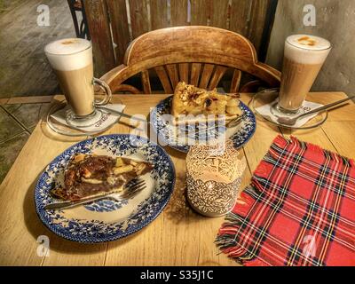 Kaffee und Kuchen auf einem rustikalen Holztisch mit einem Tischset aus Tartan und Kerze. Stockfoto