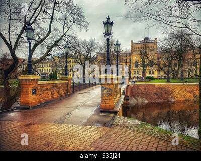 Brücke über den Fluss, flankiert von altmodischen verzierten schwarzen Laternenpfosten. Im Hintergrund als schöne goldfarbene historische Gebäude, die den Kühlschrank ergänzen. Bäume.“ Stockfoto