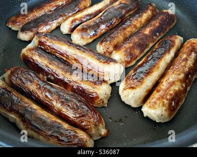 Nahaufnahme von frischen Cumberland Schweinefleisch Würstchen sizzling in einer Pfanne. Fettige und leckere Speisen. Traditionelles englisches Fleischfrühstück in einer großen Pfanne. Stockfoto