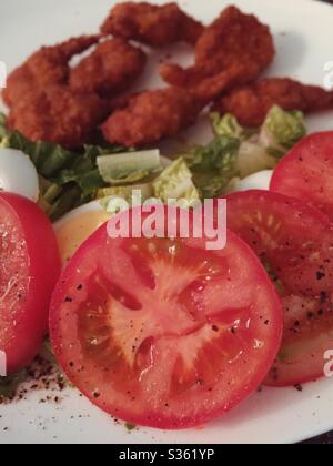 Ein Hauptgericht mit panierten, gebratenen Garnelen und einem frischen Gartensalat mit geschnittenen, von Weinreben gereiften Tomaten Stockfoto