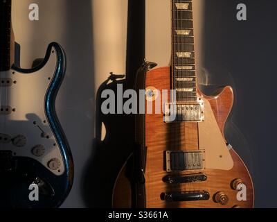 Gibson (braun) und Fender (blau Custom Shop) Gitarren an der Wand durch das Sonnenlicht in einem Studio gebadet. Stockfoto