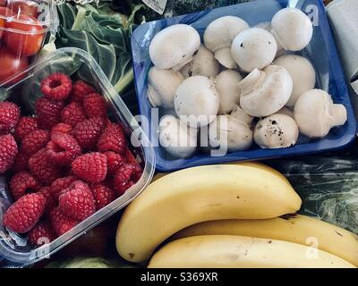Nahaufnahme von frischem Obst und Gemüse, das den Rahmen mit gesunden Farben füllt. Himbeeren, Bananen, Pilze und Salatgemüse in einer Kiste mit gemischten Früchten und Gemüse. Stockfoto