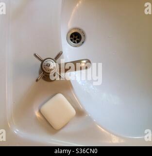 Weißes Waschbecken mit heißem Wasserhahn aus Vintage-Gold und weißem Seifenstück Stockfoto