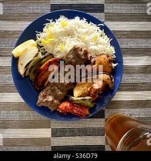 Blick von oben auf den Teller mit Kebab-Fleisch, gegrilltem Gemüse und weißem Reis. Ein Glas Bier an der Seite Stockfoto