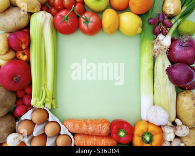 Lebendige und farbenfrohe Obst- und Gemüsesorten bilden einen quadratischen Rahmen mit Kopierfläche vor einem pastellgrünen Hintergrund. Frische und biologische Lebensmittel von einem lokalen Bauernmarkt. Stockfoto