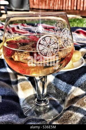Glas Gin Tonic mit Eis und Himbeeren auf einem Picknickteppich im Garten Stockfoto