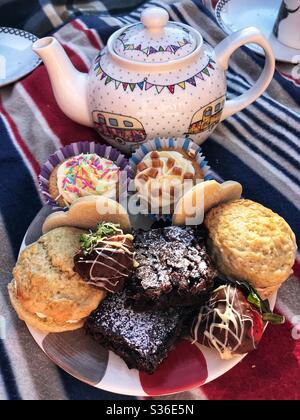 Teller mit Kuchen und eine Teekanne auf einem Picknickteppich im Garten Stockfoto