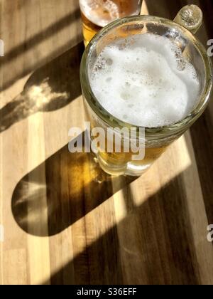 Glas Becher Bier auf einer Holzoberfläche mit Sonnenlicht durchscheint Stockfoto