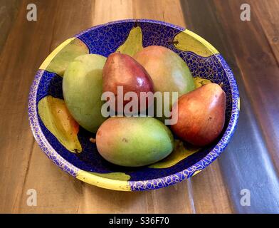 3 Mangos und 2 Anjou Birnen in einer handbemalten hölzernen Obstschale. Stockfoto