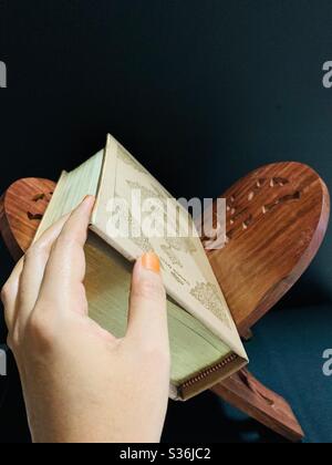 Goldener Heiliger Koran mit Quran Holzständer mit Hand aka Rihal mit schönen Kunstwerken mit dunklem Hintergrund & Seitenlicht und Schatten davon, vor der Rezitation Stockfoto