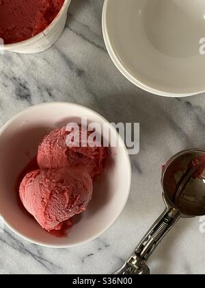 Himbeer-Eis in Schüssel mit Schaufel in Marmor Arbeitsplatte Stockfoto