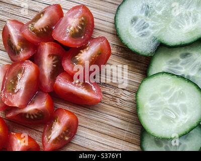 Nahaufnahme von frisch zubereiteten Salatzutaten zum Abendessen. Gesunde Tomaten und Gurken. Gewaschen und gespült. Geschnitten, gehackt und geviertelt auf einem rustikalen Holzbrett Stockfoto