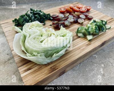 Nahaufnahme von frisch zubereiteten Salatzutaten zum Abendessen. Gesunde rote Trauben, Salat, Tomaten, Gurken. Gewaschen und gespült. Geschnitten, gehackt und geviertelt auf einem Holzhacken Stockfoto