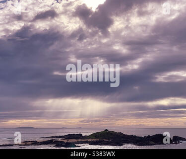 Ätherische Sonnenstrahlen, die durch ein Loch in den Sturmwolken über dem Meer platzen, auf das Meer darunter Stockfoto