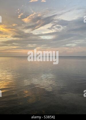 Farbenfrohe Sonnenuntergänge mit Wolken, die sich auf das noch immer in der Bucht spiegelnde Wasser spiegeln Stockfoto