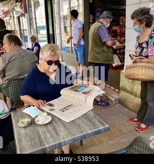 Ältere Frau beim Lesen einer Zeitung an einem Café-Tisch - Frankreich. Stockfoto