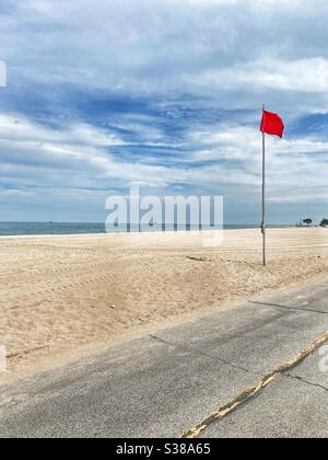 Leerer Strand mit einer roten Flagge, die das Schwimmen verbietet. Der Strand ist geschlossen und niemand darf darauf sein. Stockfoto