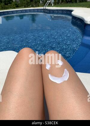 Sonnencreme, die in Form eines Smiley-Gesichts am Hinterhof-Pool auf das Bein der Frau aufgetragen wird Stockfoto