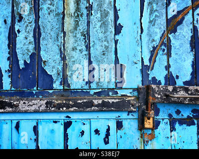 Strukturiertes altes Garagentor mit schuppiger blauer Farbe und Vorhängeschloss Stockfoto