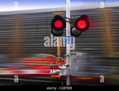 Ein Güterzug, der an einem Bahnübergang vorbeifährt, Ontario, Kanada. Rote Anzeigen blinken. Konzept, schnell und langsam, fest und in Bewegung, Gefahr nähert sich. Riskant, Vorsicht, vorübergehend, flüchtig, kurzzeitig Stockfoto