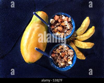 Frühstück. Zwei Schalen mit Papaya, Banane, Müsli und Honig. Eine Papaya und vier Bananen. Stockfoto