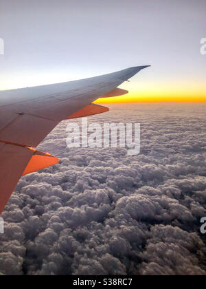 Fensteransicht von einem Flugzeugsitz mit Blick auf den Flugzeugflügel bei Sonnenaufgang mit Wolken. Stockfoto