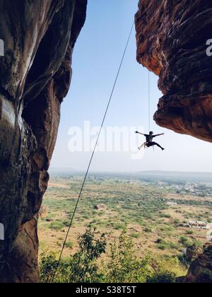 Ein Kletterer, der am Seil hängt, während er sich abseilt, nachdem er die Route auf einer Granitfelsenwand in der Nähe von Badami, Karnataka, Indien, absolviert hat Stockfoto