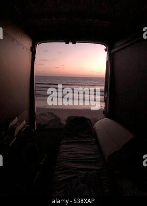 Genießen Sie einen perfekten kalifornischen Sonnenuntergang und die Aussicht auf perfekte Wellen auf der Rückseite eines Ford Transit Van, das perfekte Surfmobil. Stockfoto