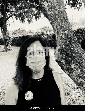 Frau, die gerade während der COVID-19 in der lokalen Primärwahl gestimmt hat, trägt einen Sticker und eine nicht-chirurgische Maske. Stockfoto