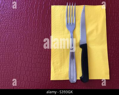 Messer und Gabel auf gelber Papierserviette Stockfoto