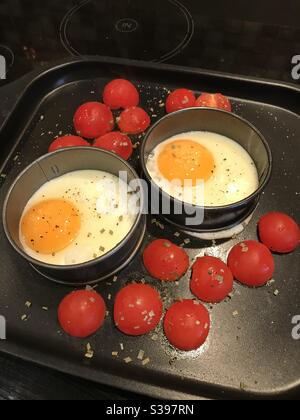 Spiegeleier in kreisförmigem Ring mit Tomatentomaten und Kräutern Auf Backblech Stockfoto