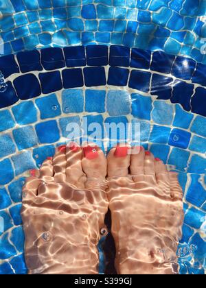 Frauenfüße im Wasser auf Schwimmbadstufen Stockfoto