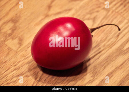 Eine einzelne rote reife Tamarillo-Frucht liegt auf einer hölzernen Platine Stockfoto