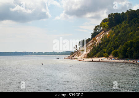 Ostseeküste bei Sellin auf der deutschen Insel Rügen mit bewölktem Himmel im Sommer. Schwimmer, SUP und Touristen im Wasser und am Strand Stockfoto