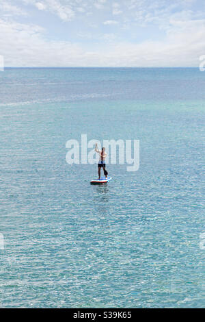 Ein Stand Up Paddler SUP mit blauen Badehosen an Das offene Meer auf dem blau türkisfarbenen Wasser und unter Ein leicht bewölktes Himmel Stockfoto