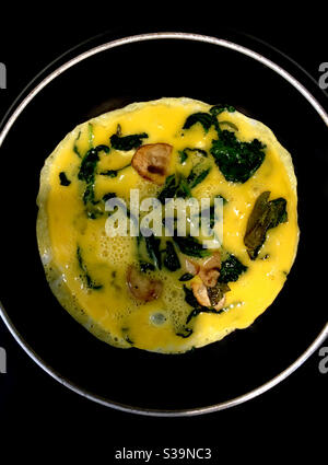 Eier kochen in einer Pfanne auf dem Herd mit Spinat und Champignons. Stockfoto