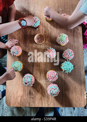 Gruppe von Kindern backen Cupcakes, Vorbereitung Zutaten, Toppings, Streuseln für die Dekoration Cookies. Kinder lernen zu kochen, arbeiten zusammen in der Küche zu Hause. Konzept der glücklichen Familie Stockfoto