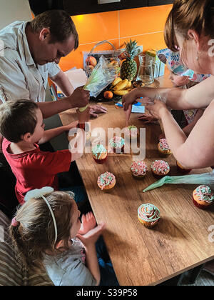 Gruppe von Kindern backen Cupcakes, Quetschen Sahne aus Süßwarenbeutel, Zutaten vorbereiten, Belag, Streuseln für die Dekoration von Cookies. Kinder kochen, arbeiten zusammen in der Küche zu Hause Stockfoto